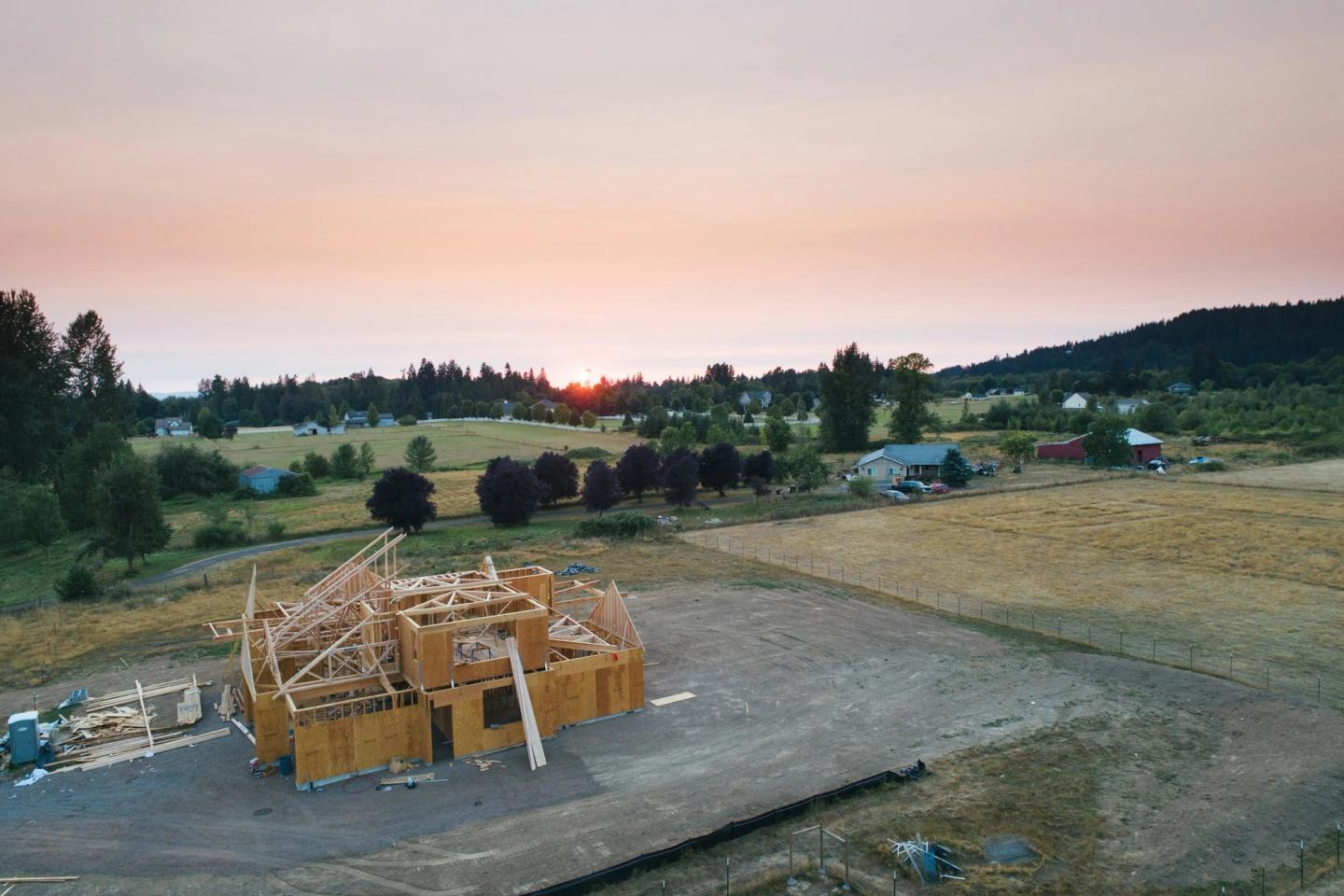 Aerial view of a wood-framed house going up on an open lot at sunset.