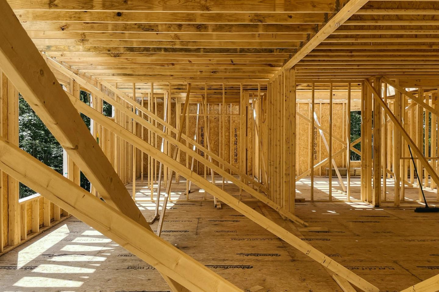 Sunlight through the open walls of a house at framing stage, with temporary bracing across the floor.