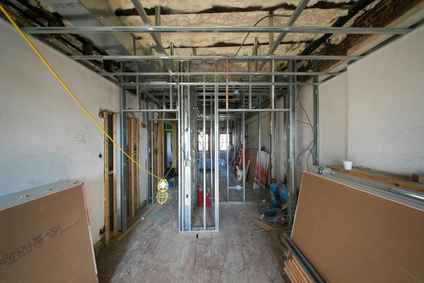 Corridor of steel stud framing with drywall sheets stacked on both sides, before the walls are closed