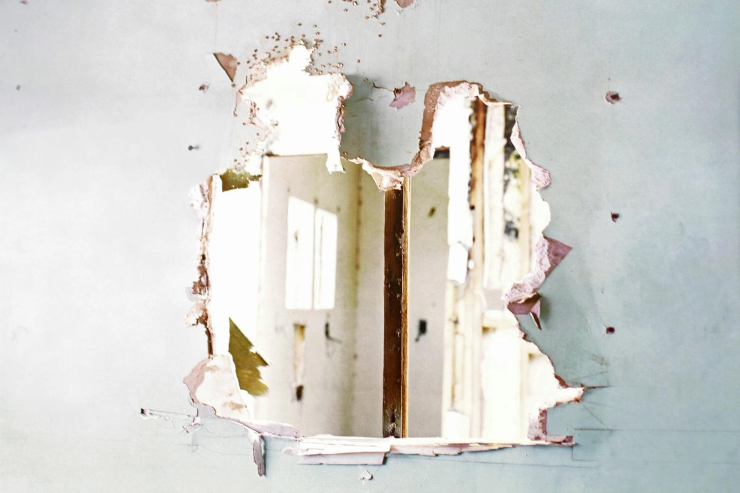 A ragged hole broken through a white drywall wall.