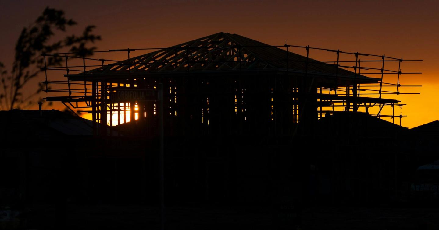 A house at framing stage in silhouette against an orange sunset.