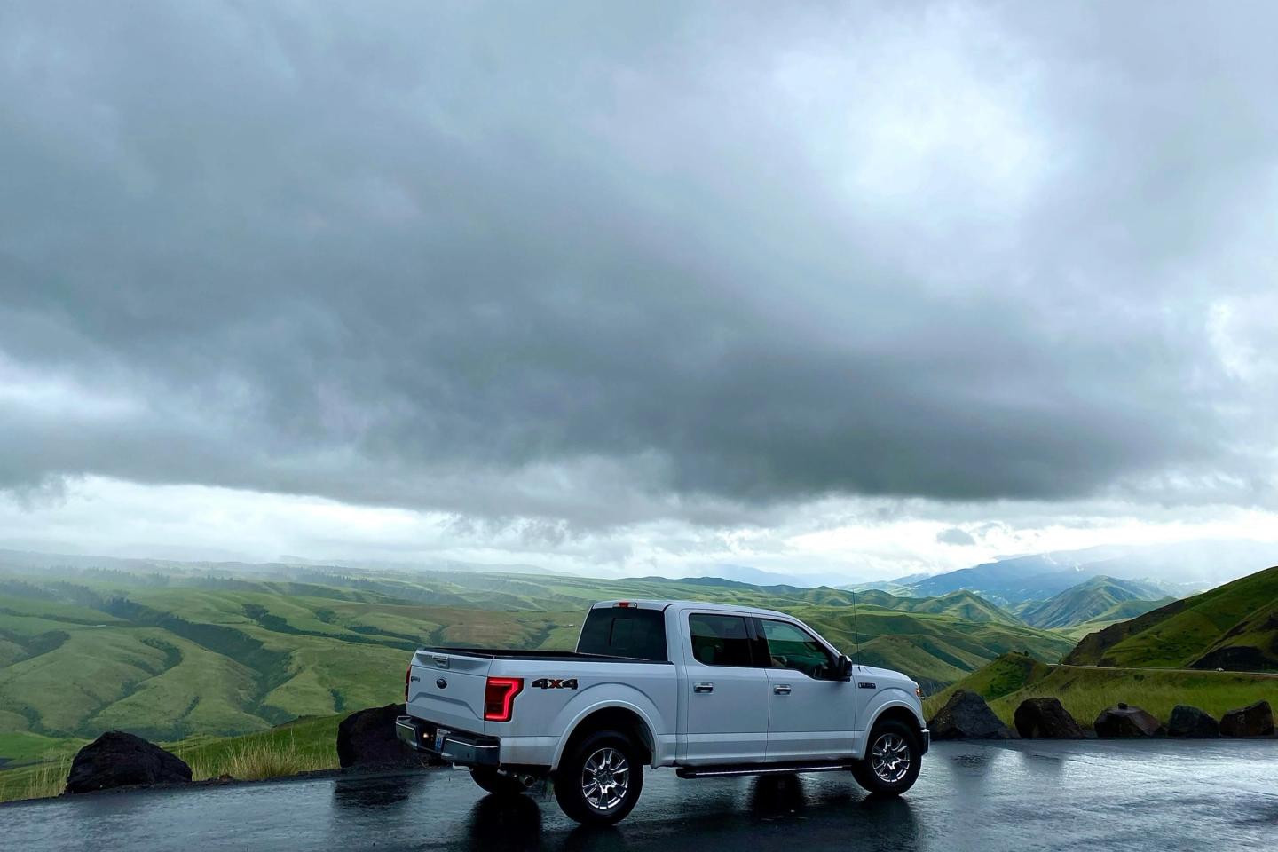 A white pickup truck parked on a wet road among green hills under heavy cloud.