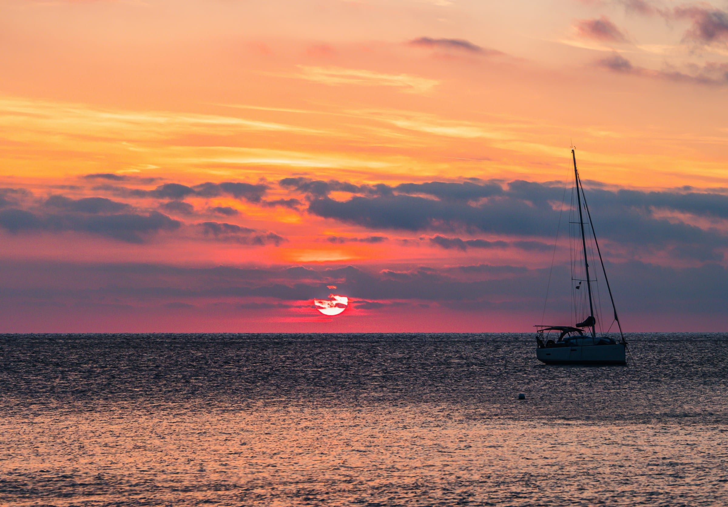 Een zeiljacht ligt voor anker op zee bij zonsondergang, onder een oranje en roze lucht