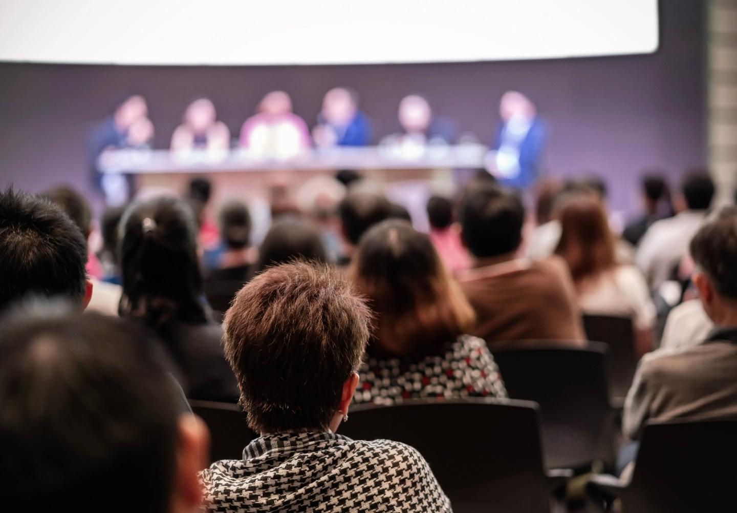 Conference attendees listening to expert panel on stage in medical conference hall