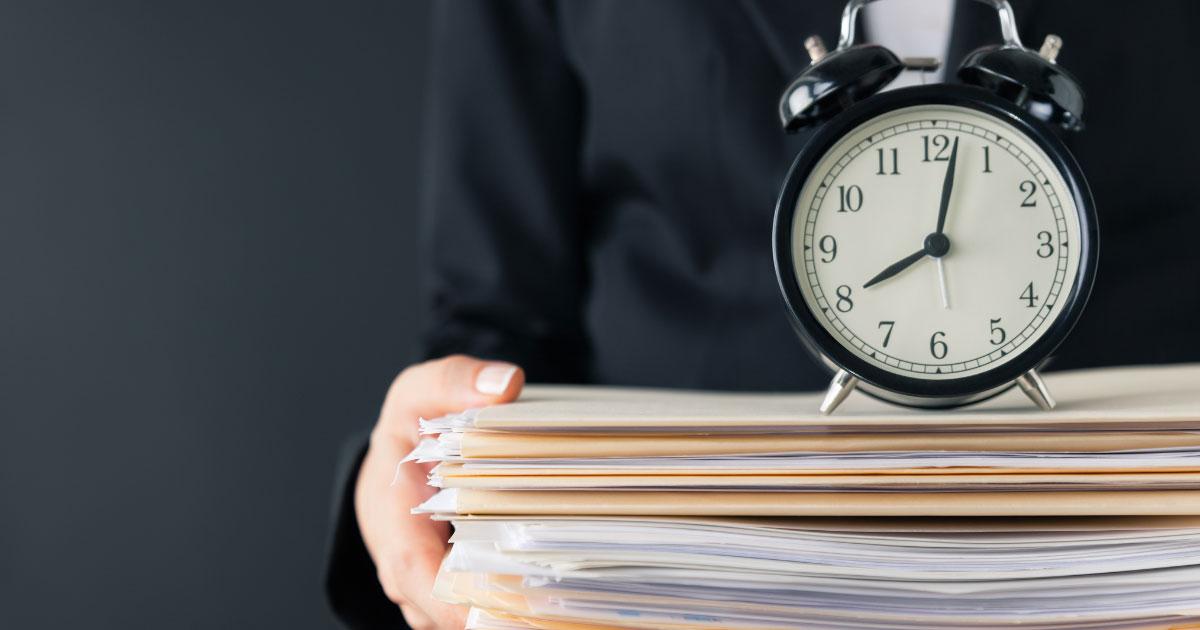 Wecker auf Aktenstapel – Symbolbild für Arbeitszeiterfassung im Unternehmen