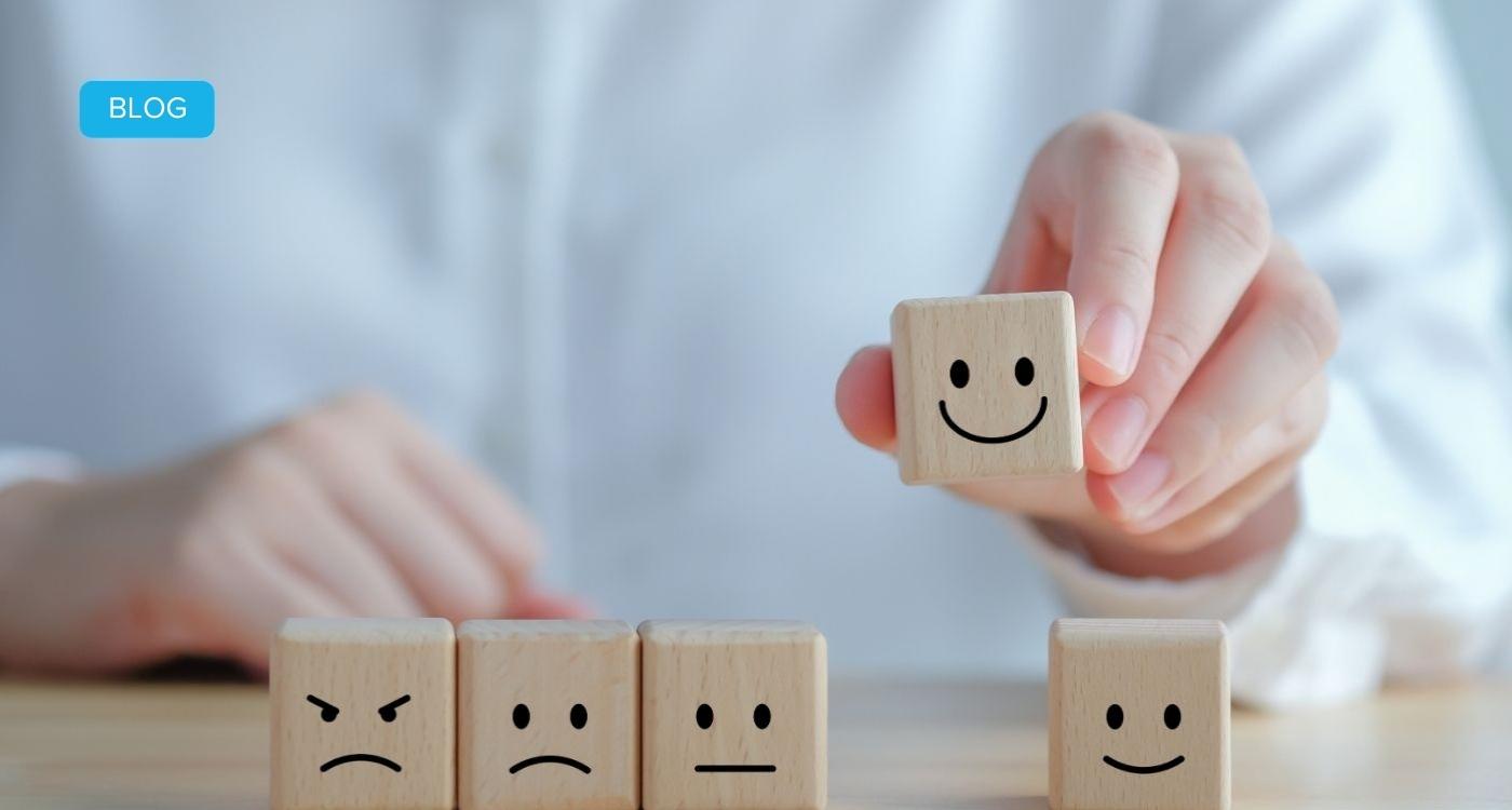 Hand wählt lächelnden Holzwürfel aus Reihe verschiedener Emotionen – Symbolbild für Employee Experience Management