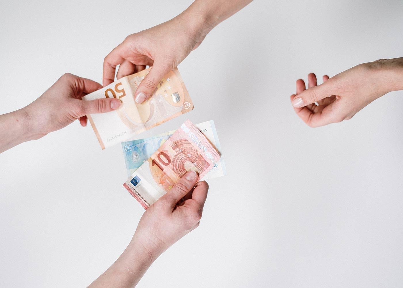 Hände tauschen unterschiedliche Geldscheine – Symbolbild für Lohnungleichheit und den Gender Pay Gap in Deutschland