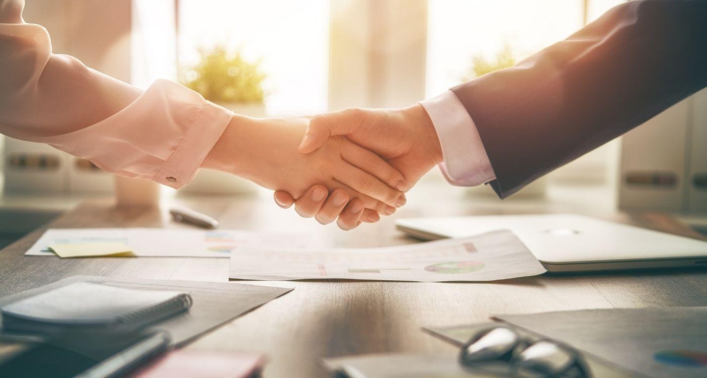 Geschäftshändedruck über Schreibtisch mit Dokumenten – Symbolbild für erfolgreiche Partnerschaft im Payroll-Outsourcing