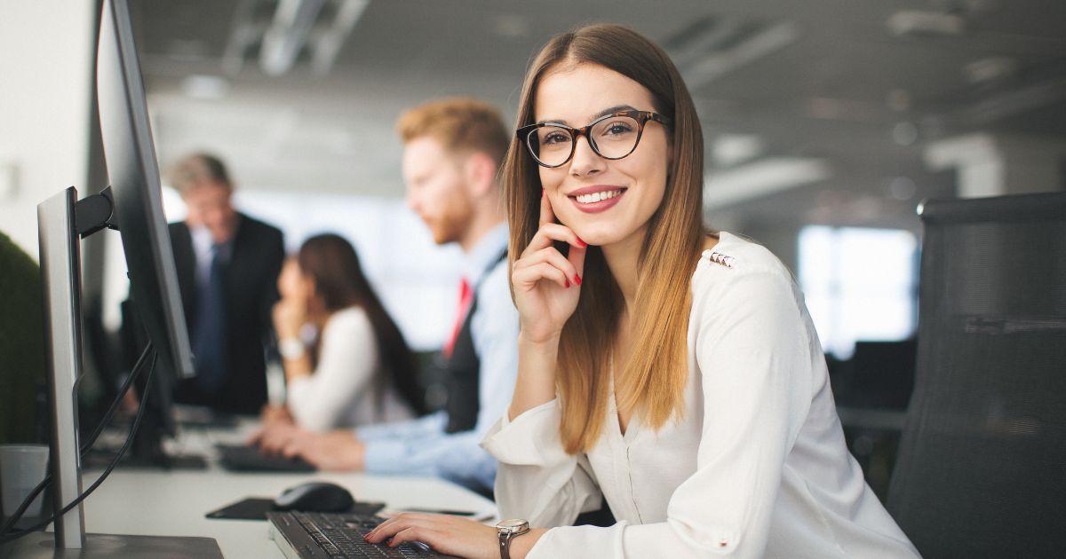 Lächelnde Mitarbeiterin am Computer im Büro – Symbolbild für effiziente Entgeltabrechnung mit dem SAP Payroll Control Center