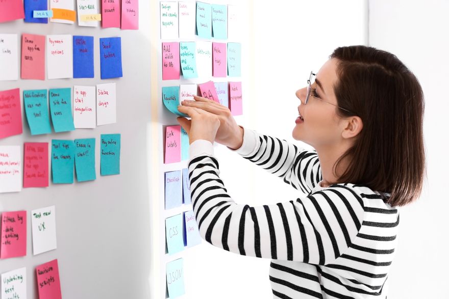 software development methodologies: Woman posting sticky notes on the office board
