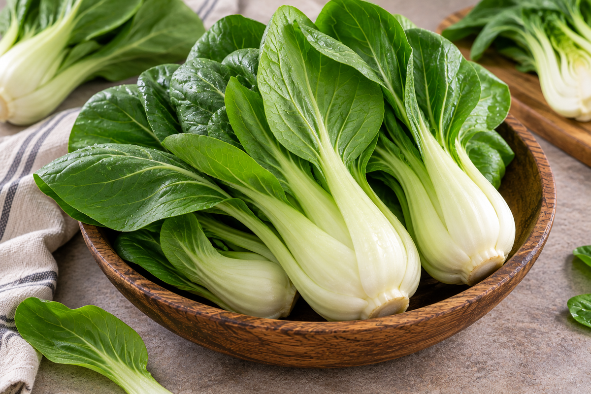 Fresh bok choy with crisp white stalks and vibrant green leaves arranged in a rustic wooden bowl.