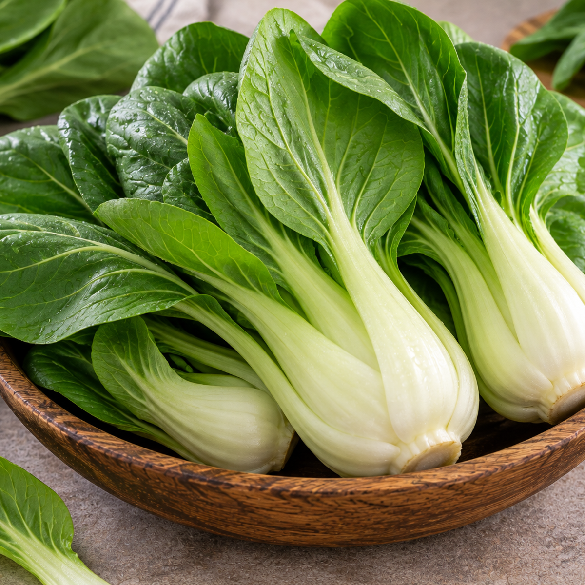 Fresh bok choy with crisp white stalks and vibrant green leaves arranged in a rustic wooden bowl.