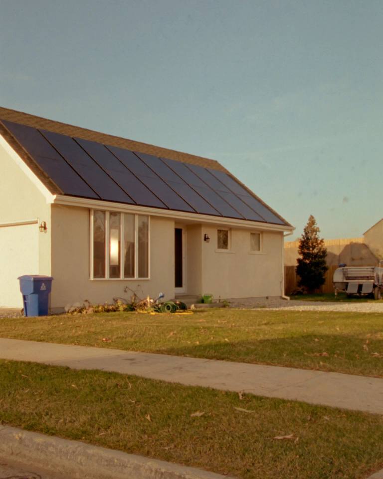 A home with rooftop solar panels catching low golden evening sun.