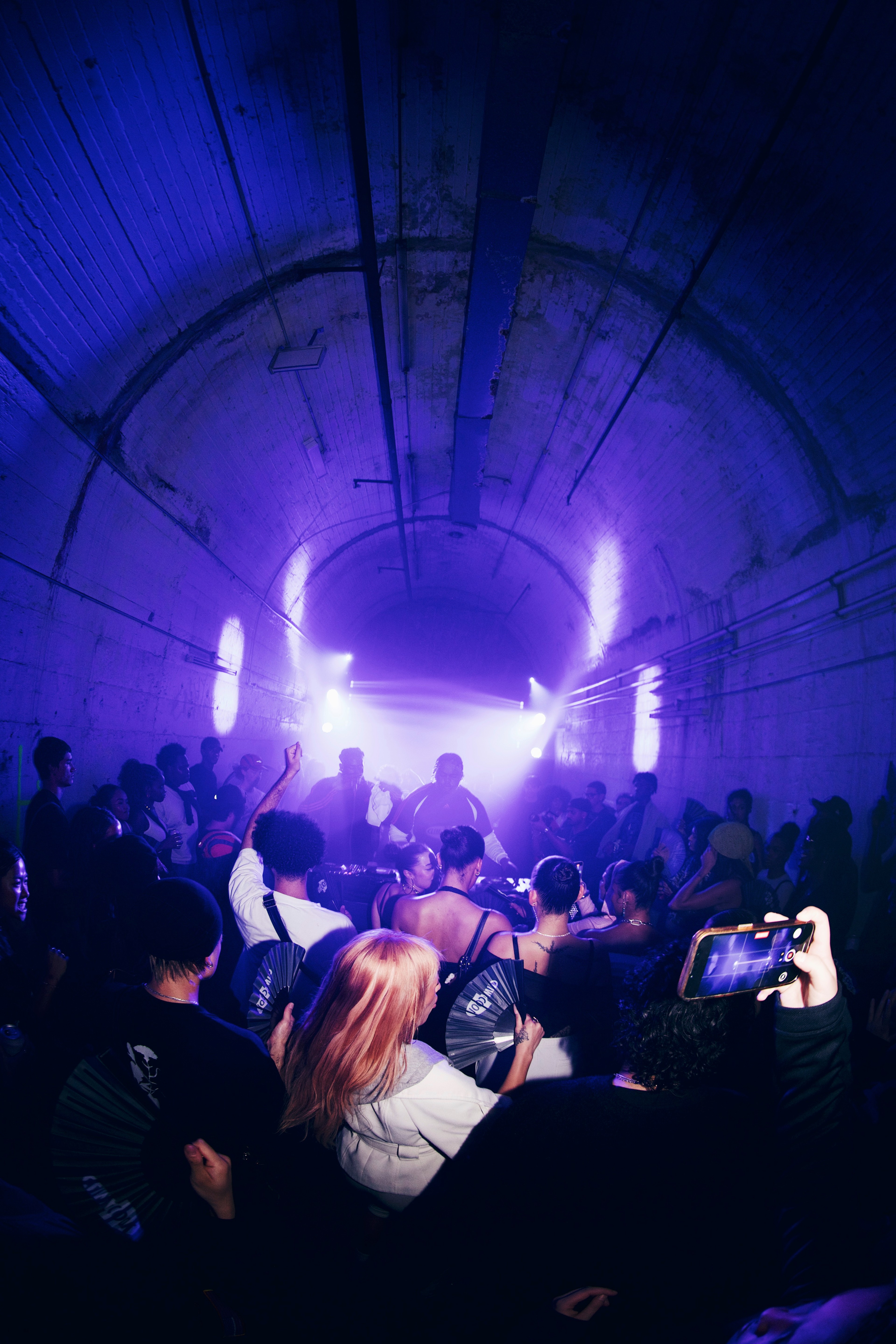 Wide view of the Wynyard Tunnels packed with crowd, stage lights beaming purple through the arched space