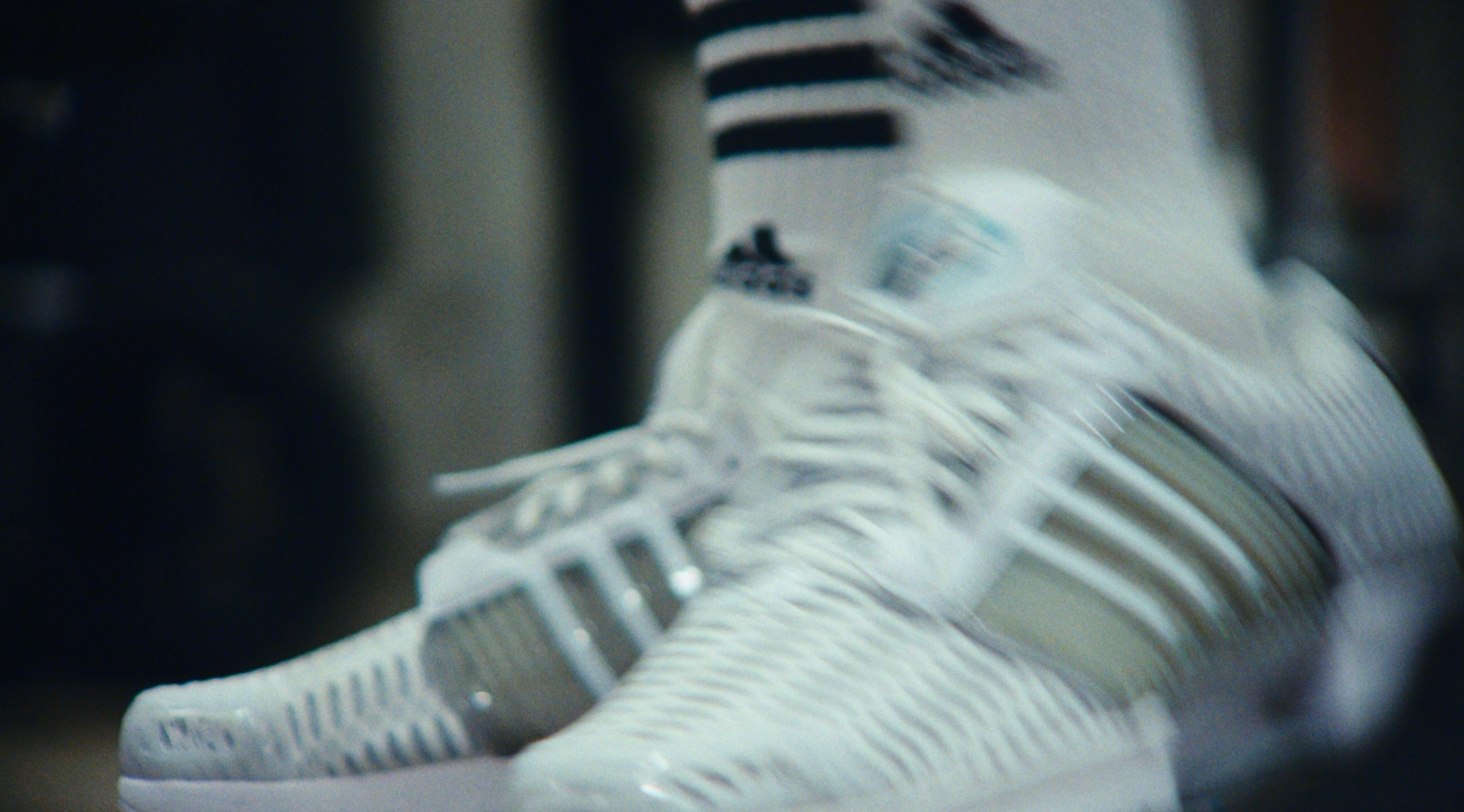 Motion-blurred close-up of white adidas CLIMACOOL sneakers worn with white socks and a black-striped sock band