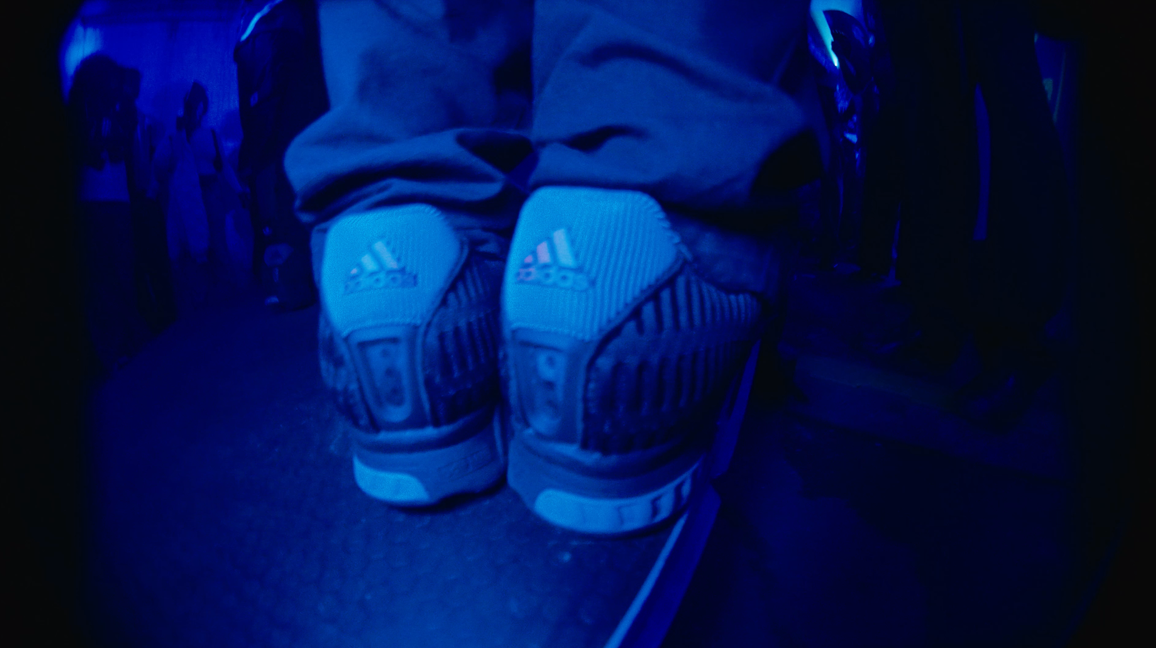 Low, fisheye-style angle of a figure in red trackpants wearing white adidas CLIMACOOL sneakers inside a blue-lit tunnel event