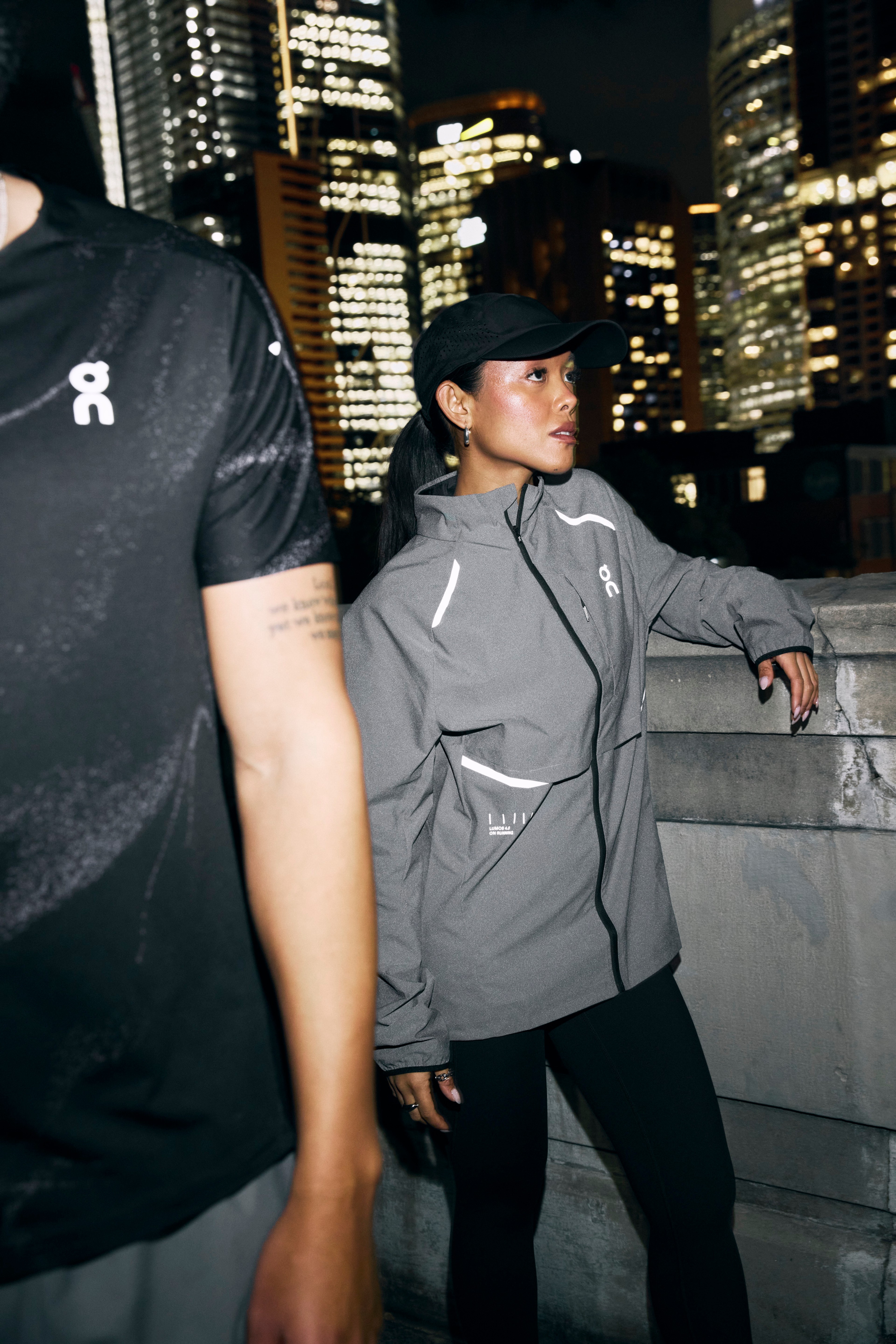 Athlete in a reflective On jacket and cap with city lights in the background