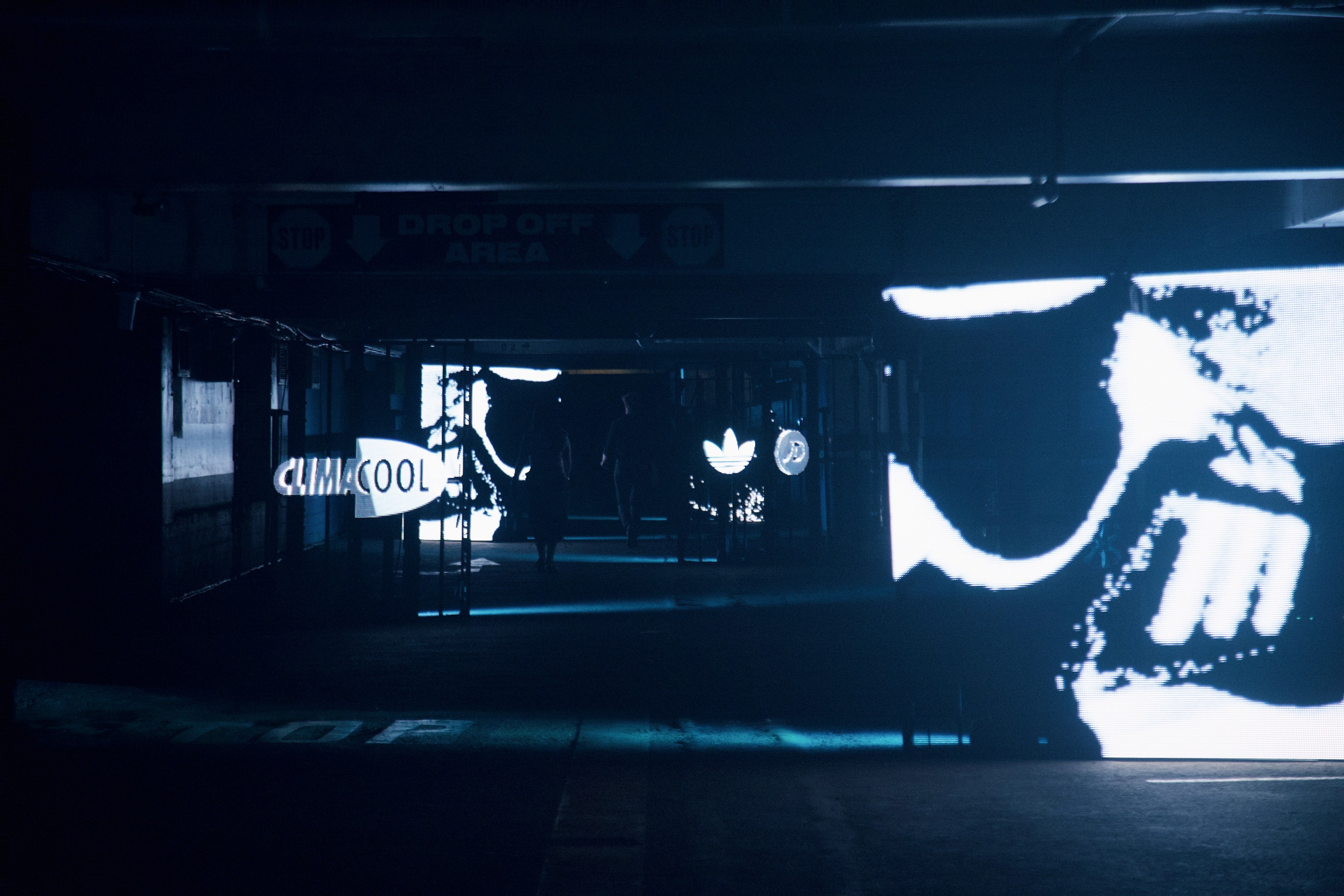 Cinematic low-light shot of the CLIMACOOL event entrance at Wynyard Station — a Drop Off Area sign, an adidas trefoil and a large illuminated CLIMACOOL logo glowing in the dark