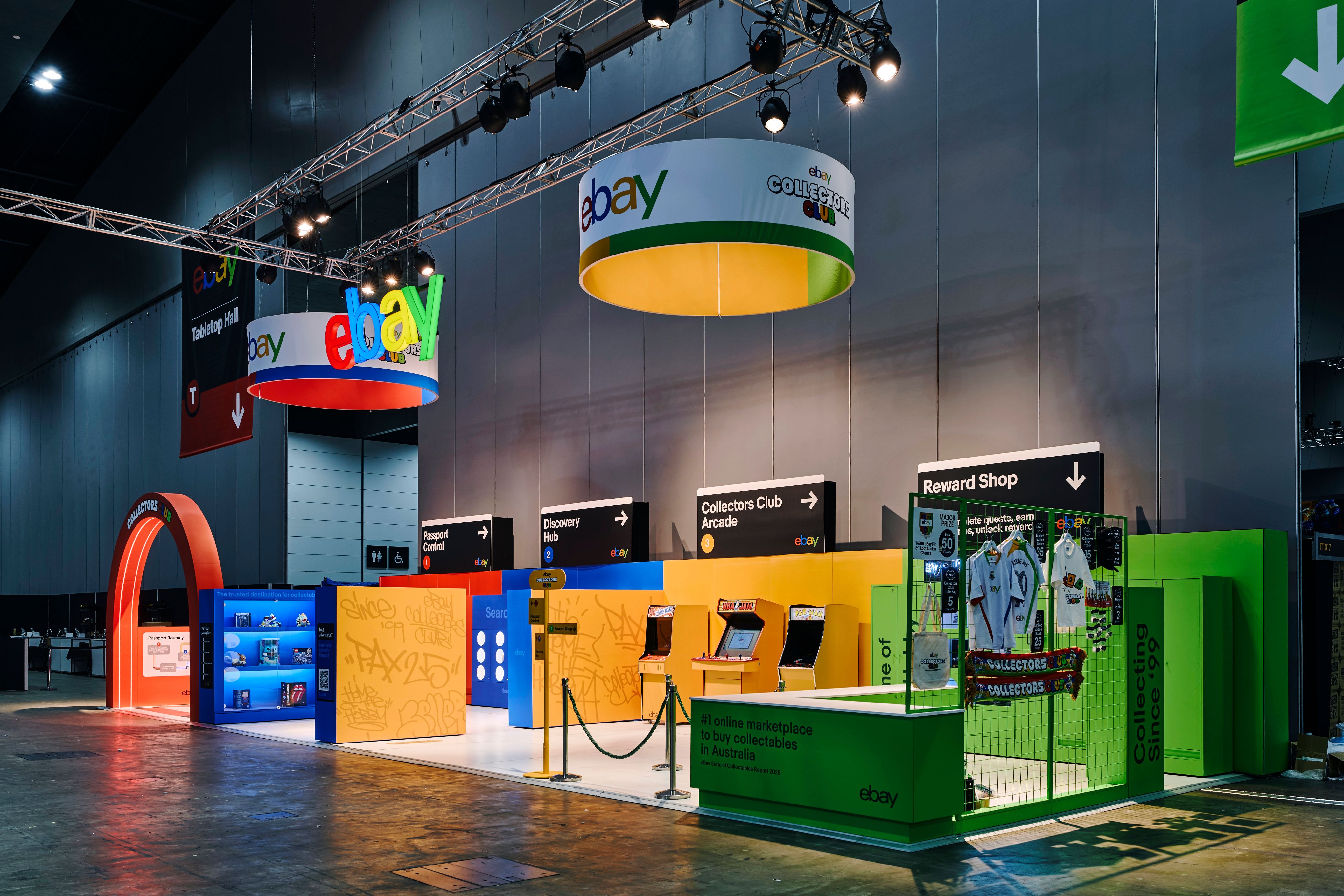Wide view of the eBay booth at PAX showing the central stage, green archway, orange and blue structural elements and surrounding merchandise displays