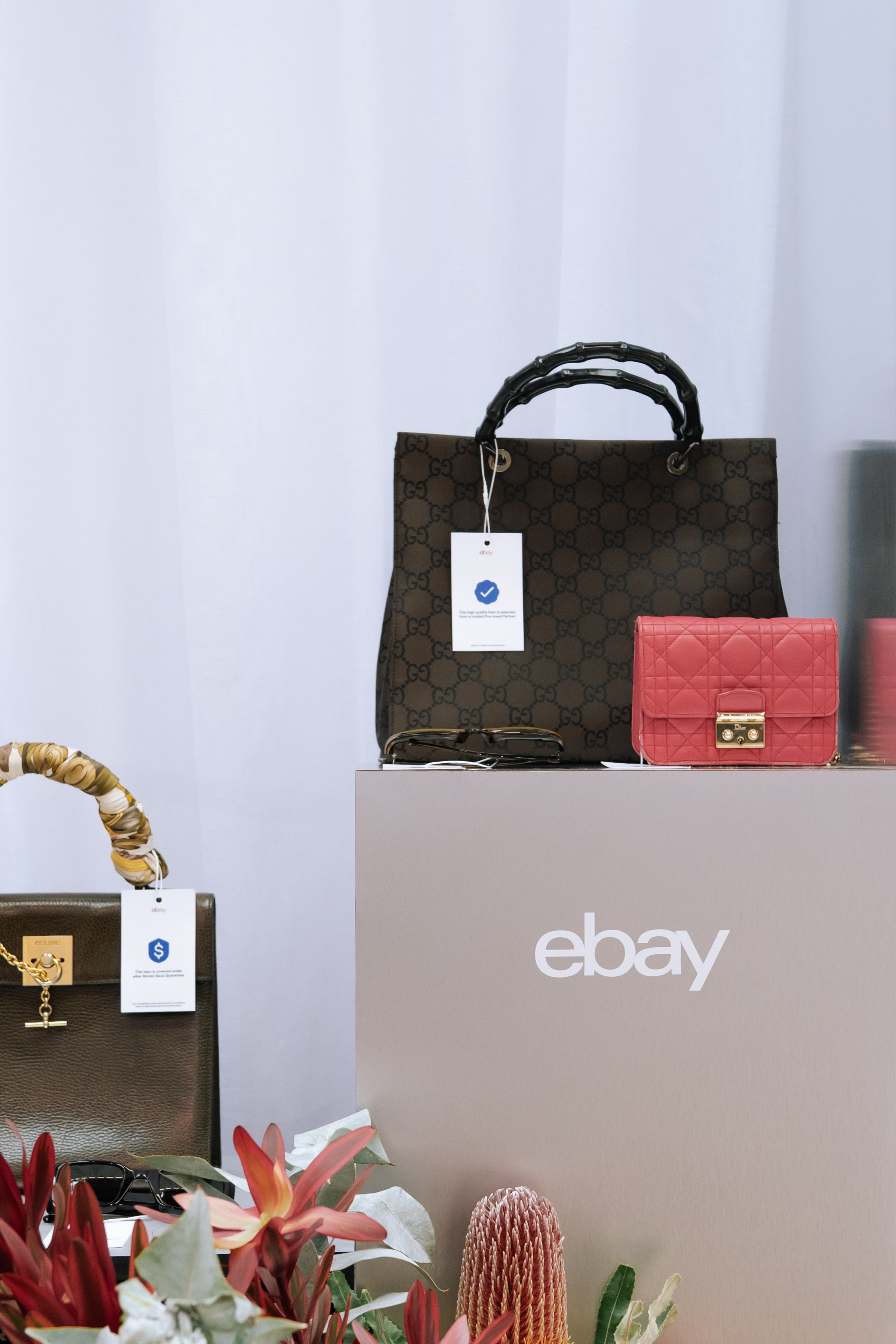 Pre-loved luxury handbags styled on a plinth with an eBay-branded shopping bag