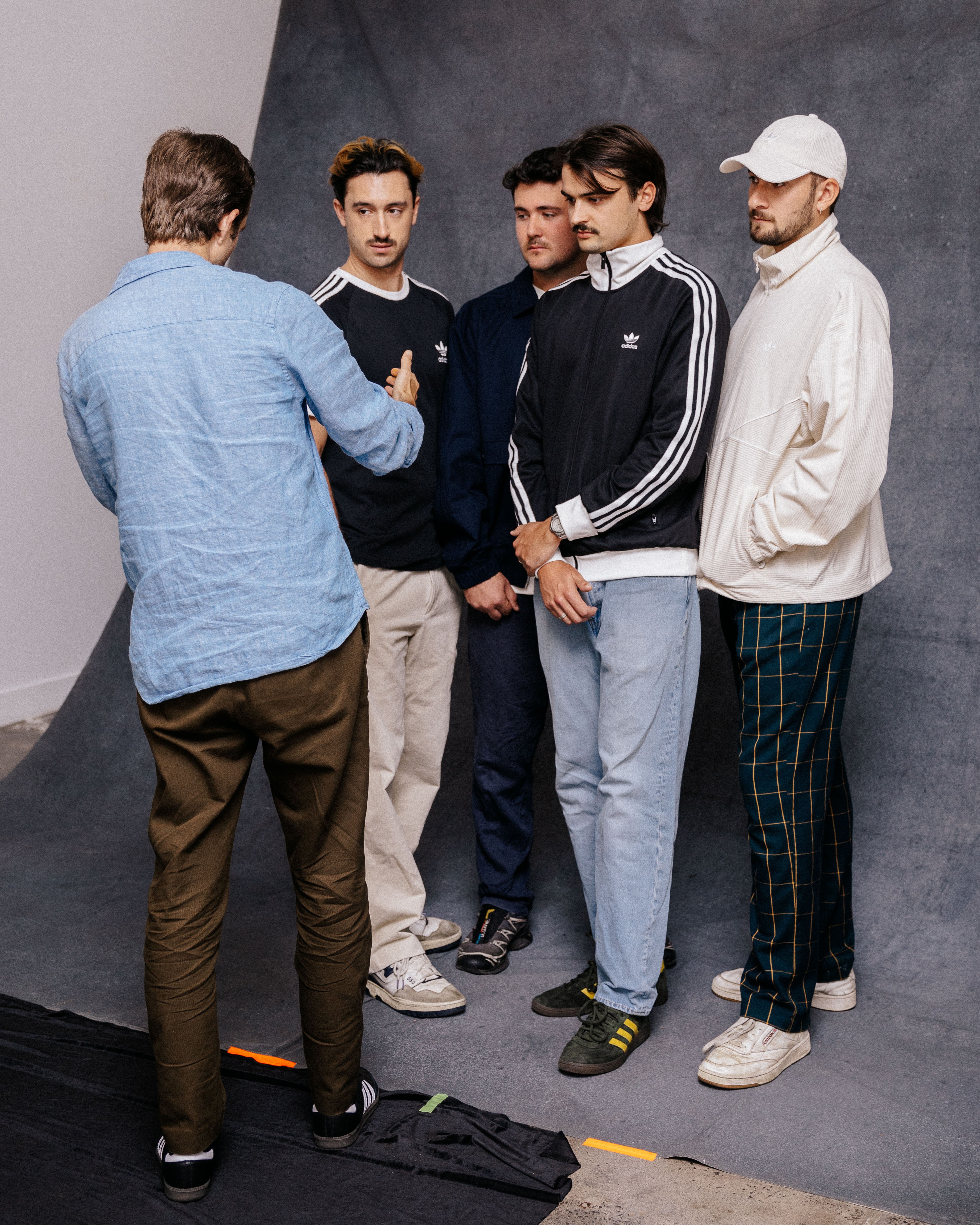 A person with their back to the camera speaks to four men standing on a grey studio backdrop.