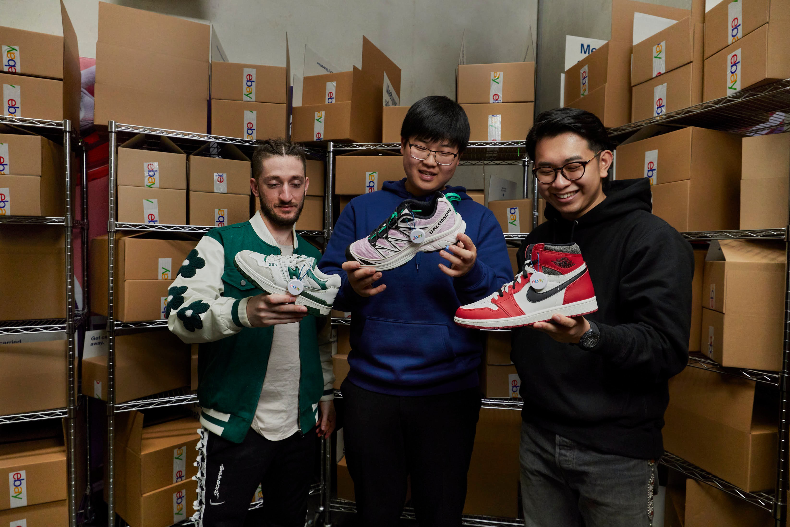 Three men displaying authenticated sneakers in an eBay warehouse.