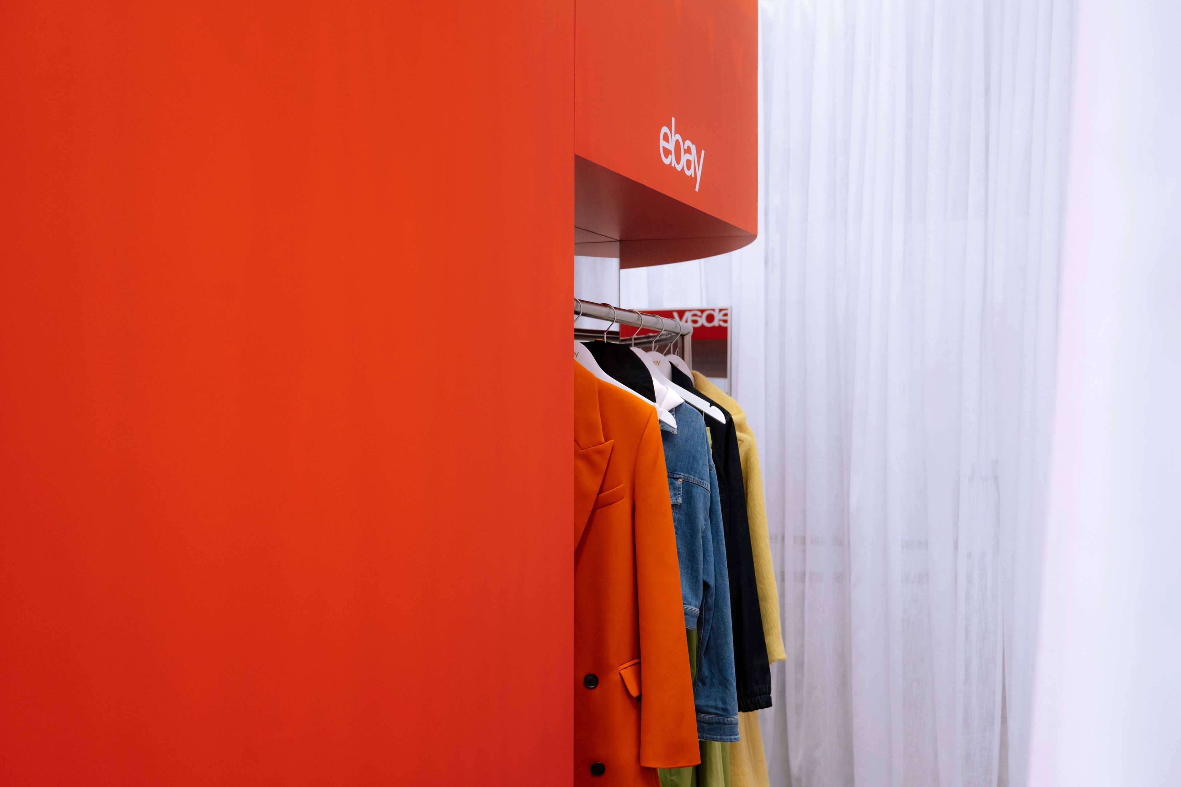 Clothing rack of curated vintage pieces in front of a bold red wall with an eBay logo overhead