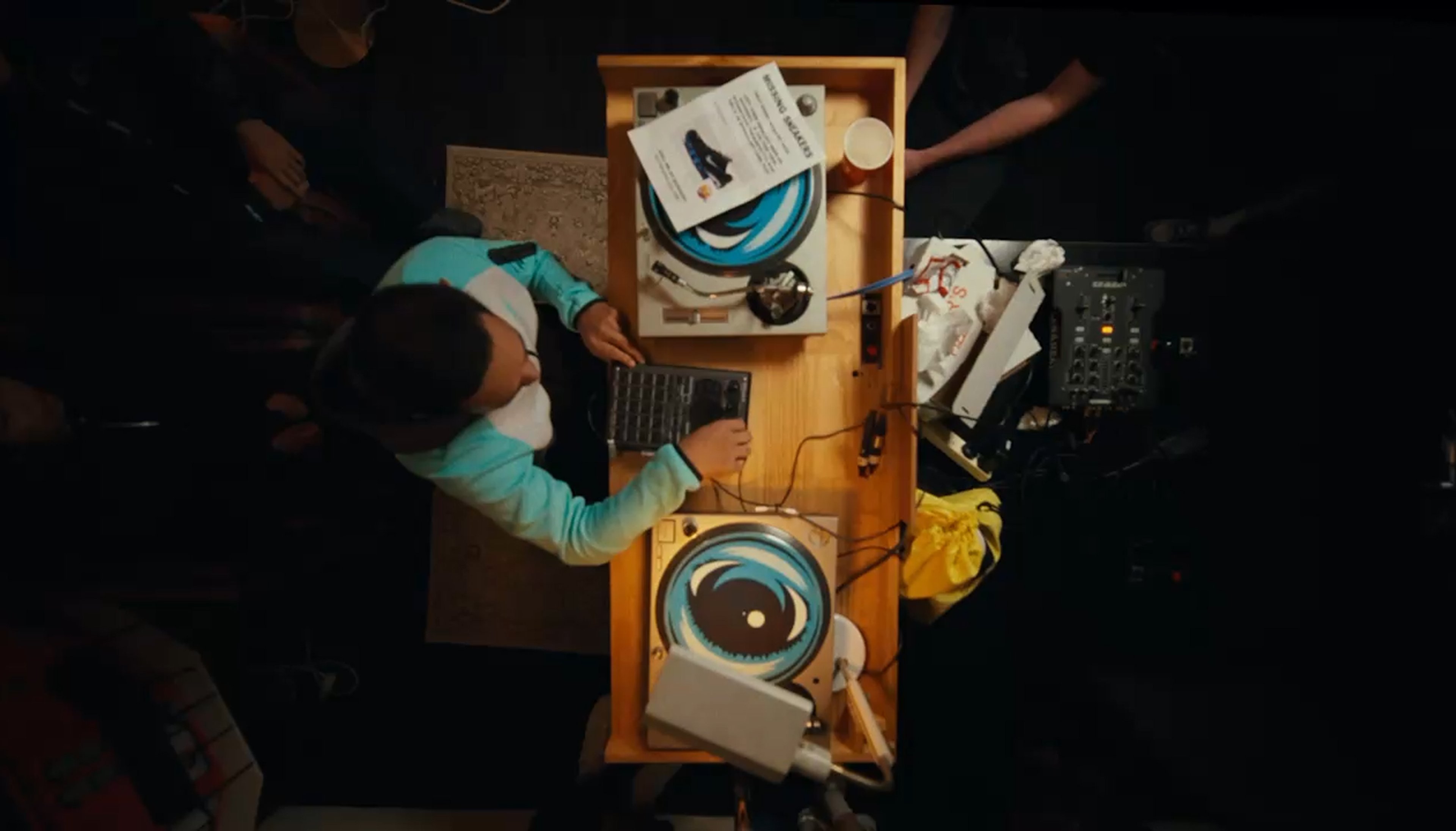 A person DJs with two turntables showing blue swirl records, a laptop, and a mixer, seen from above.