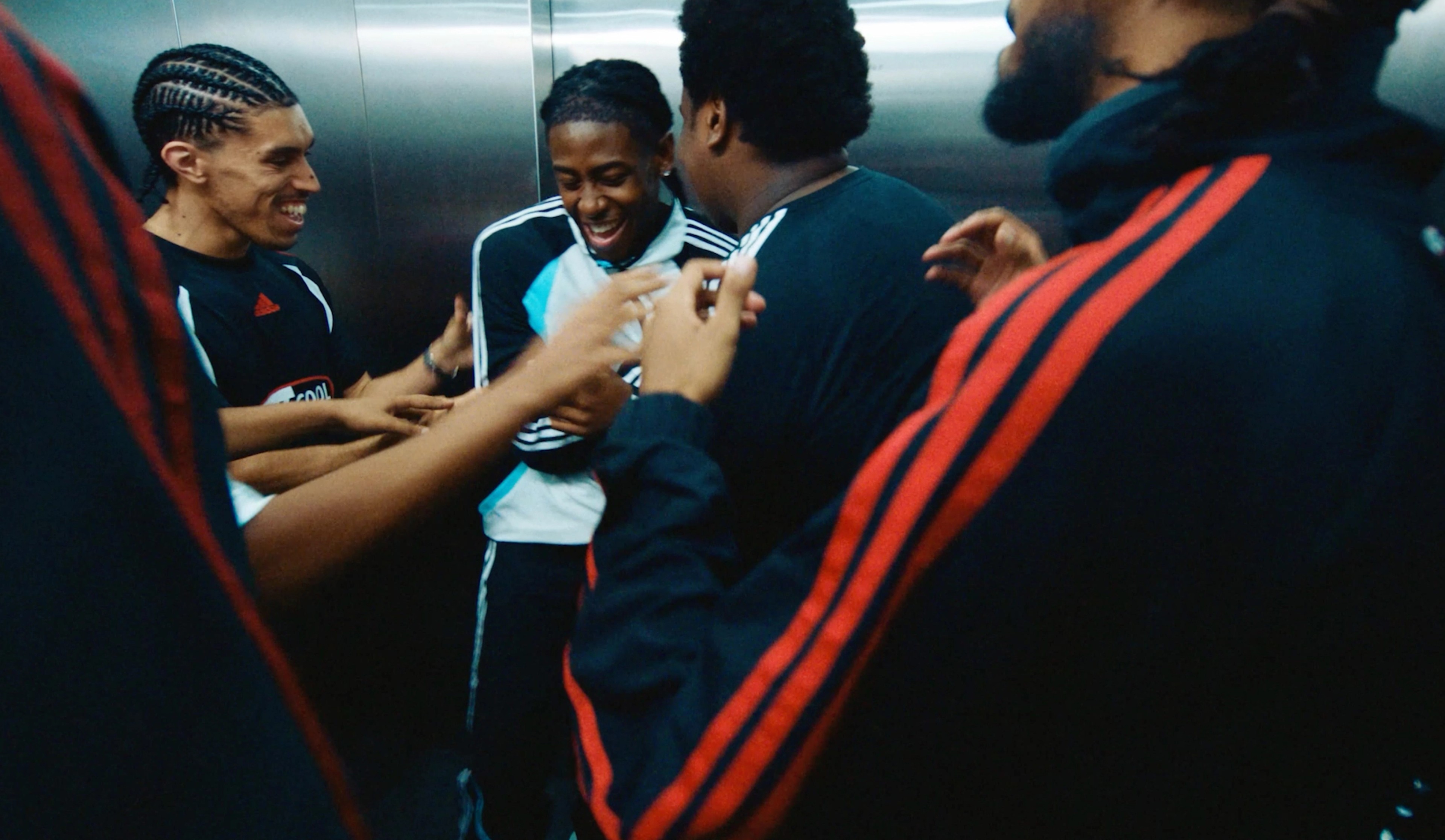 A group of young men in adidas sportswear laughing together in an elevator