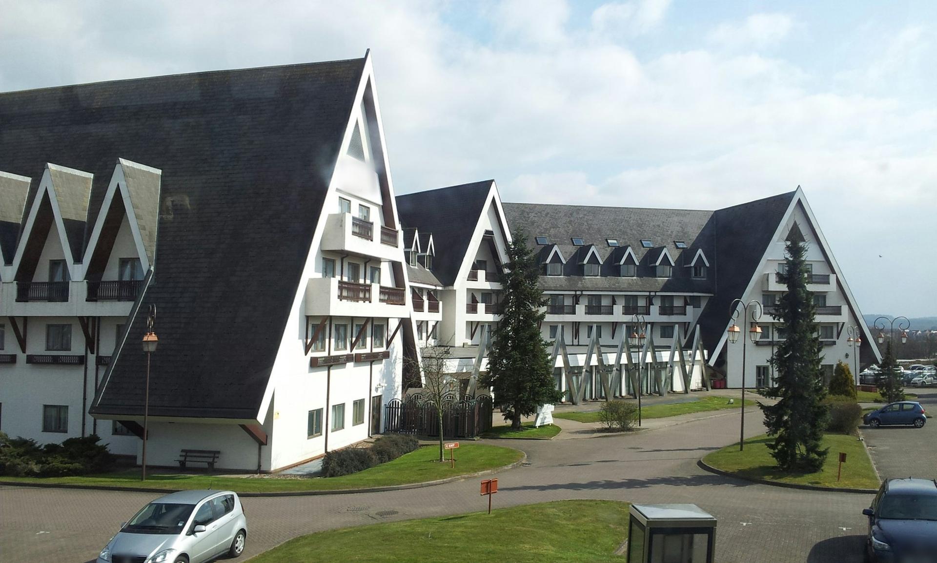 A large chalet-style hotel with steep dark roofs and white walls beside a landscaped car park in Bracknell.
