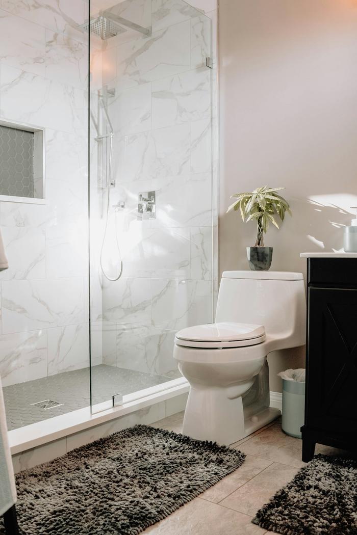 A walk-in shower with a frameless glass screen and white marble-effect tiles beside a toilet and dark vanity unit.