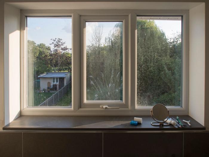 A white uPVC triple window with a dark sill, seen from inside, looking out over a garden.