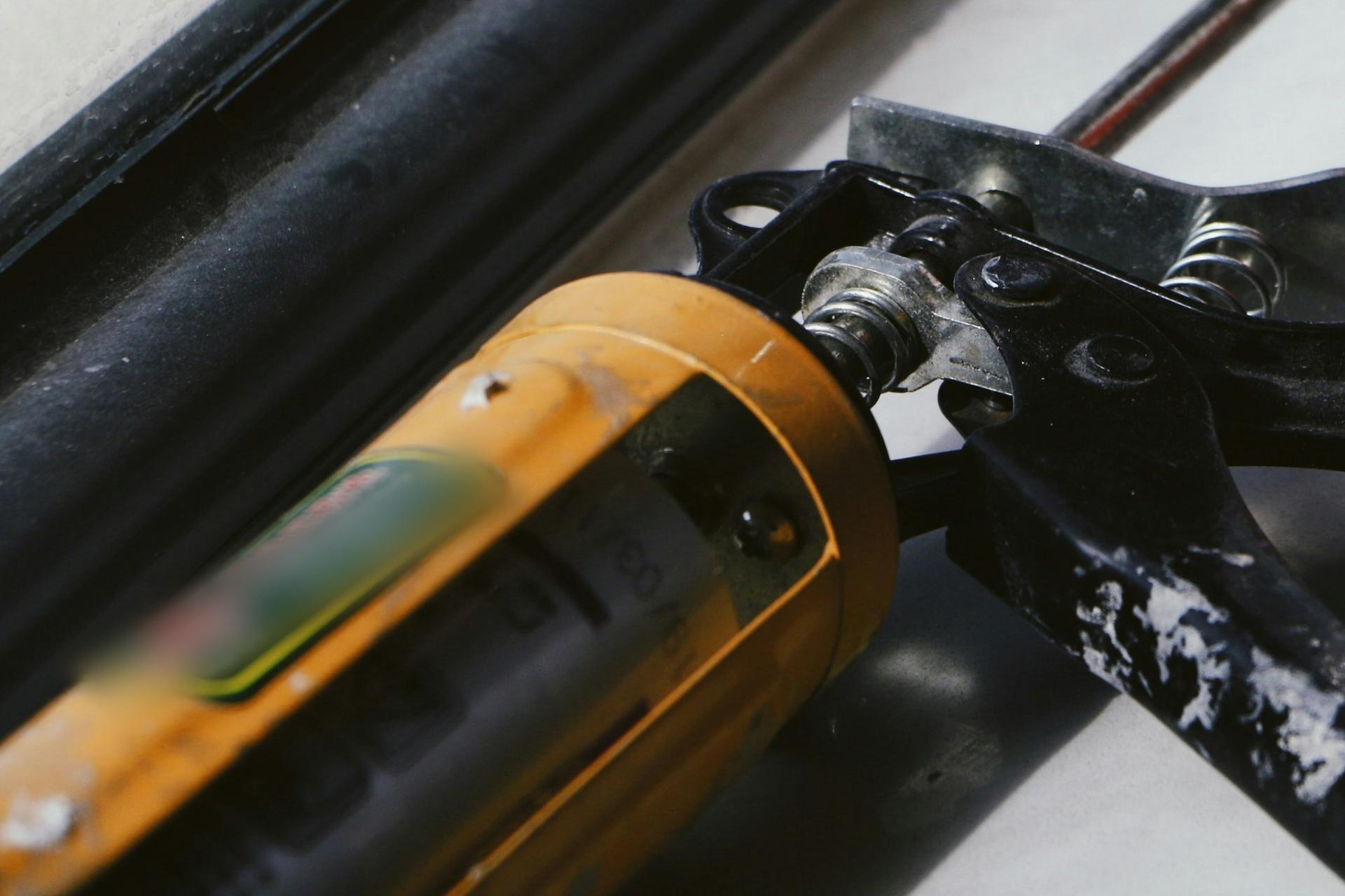 Close-up of a well-used caulking gun loaded with a yellow sealant cartridge resting on a window sill.