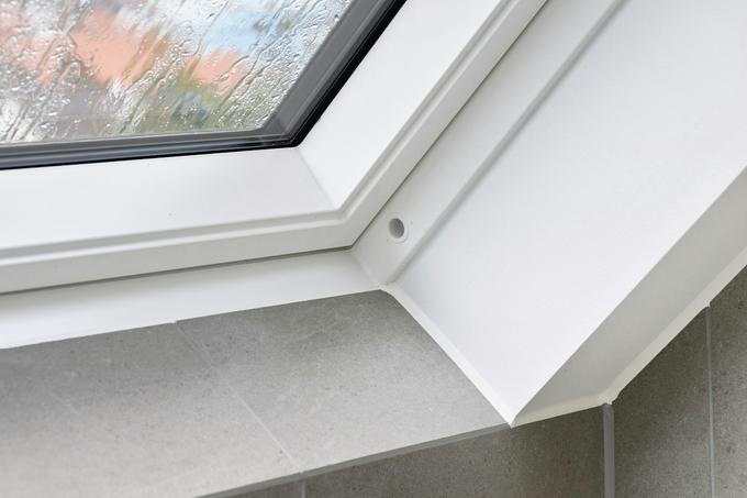 Close-up of the corner of a white uPVC window frame meeting a tiled sill, with rain on the glass.