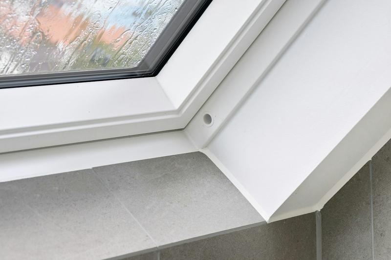 Close-up of the corner of a white uPVC window frame meeting a tiled sill, with rain on the glass.