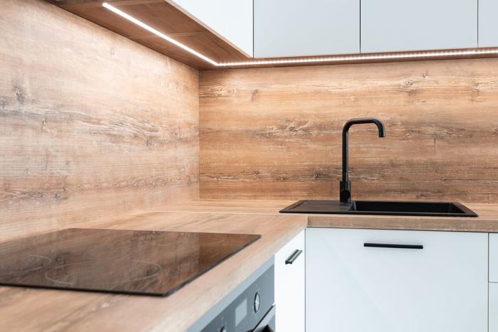 A wood-effect worktop and matching upstand meeting in a kitchen corner, with an induction hob, a black sink and a matt black tap.