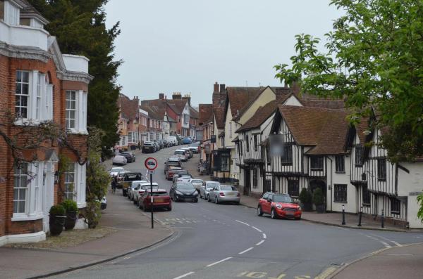 A historic English town high street with timber-framed buildings, brick houses and parked cars.