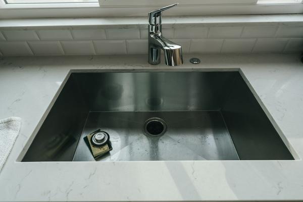 A stainless steel undermount sink set into a white quartz worktop with a chrome tap and white bevelled tile splashback.
