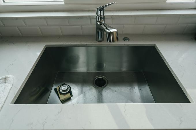 A stainless steel undermount sink set into a white quartz worktop with a chrome tap and white bevelled tile splashback.