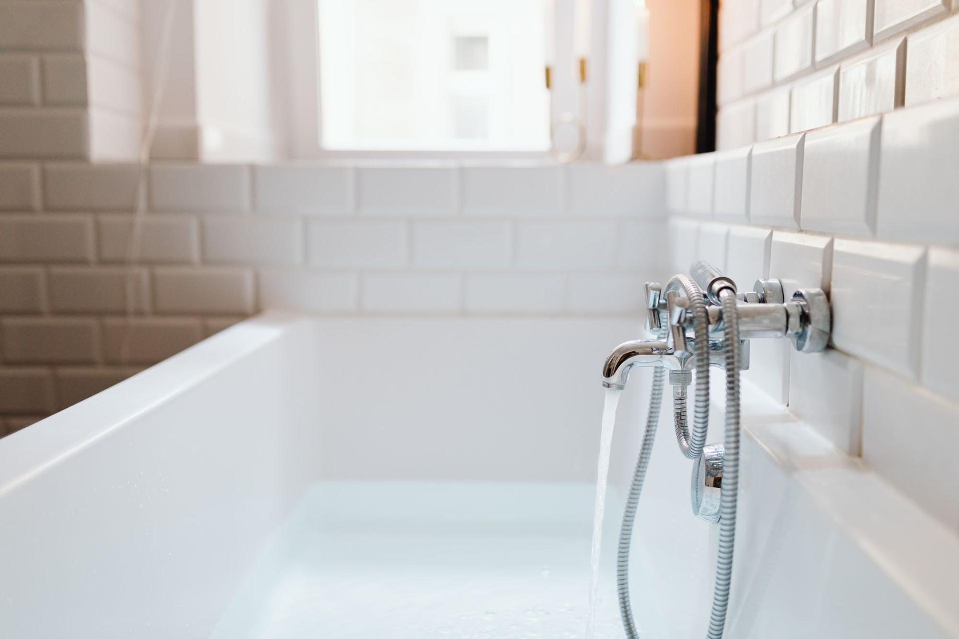 Water running from a chrome bath mixer into a white bath set against white bevelled metro tiles.