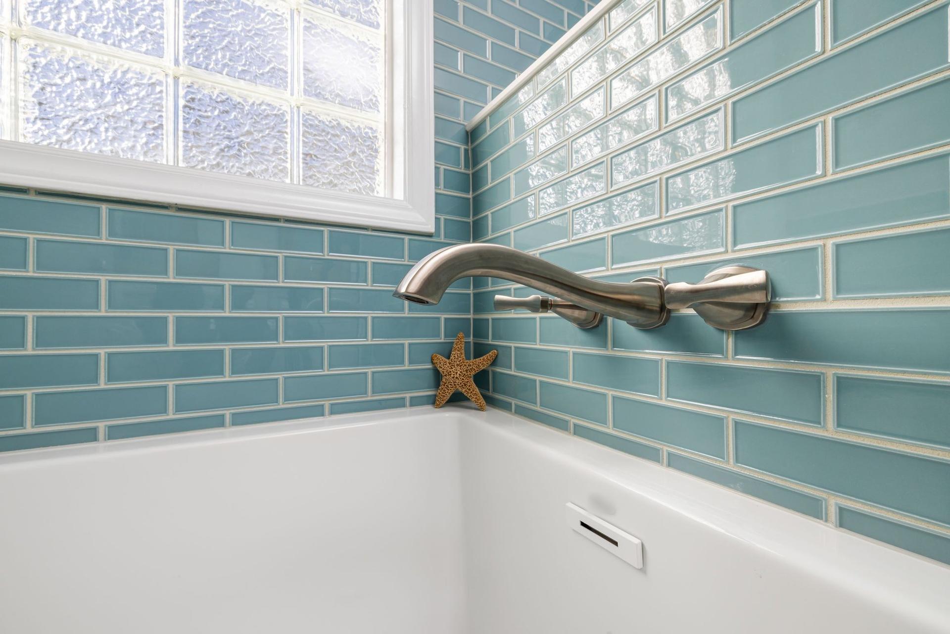 Close-up of a white bath edge meeting glossy turquoise brick-bond wall tiles, with a brushed-nickel wall-mounted tap.