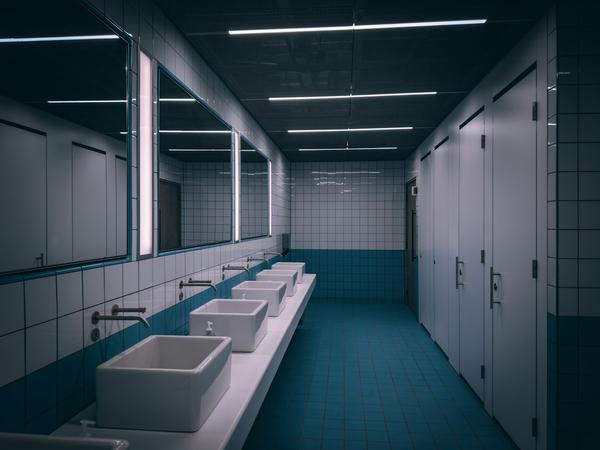 A row of square white basins with wall-mounted taps beneath long mirrors in a public washroom with teal floor tiles and white cubicle doors.