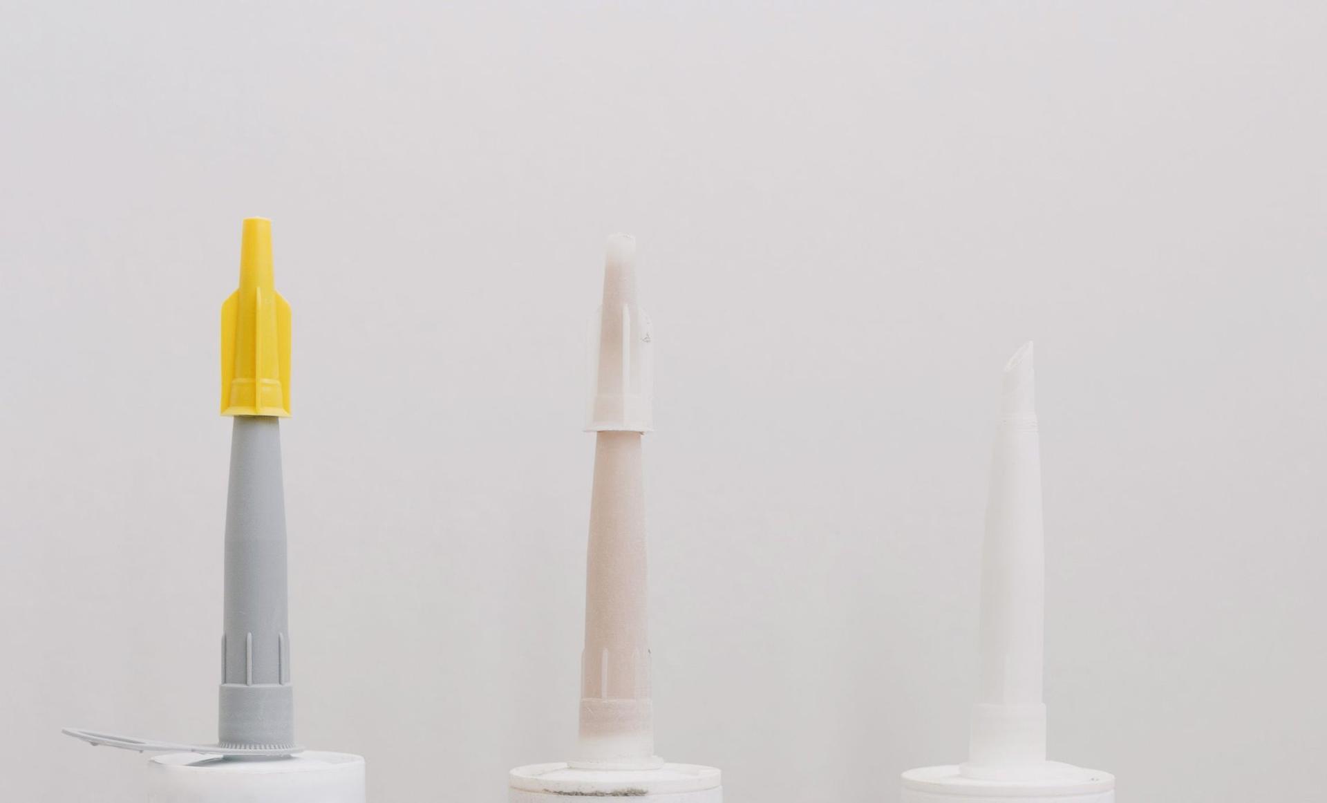 Three sealant cartridges with cut applicator nozzles lined up against a plain pale grey wall.