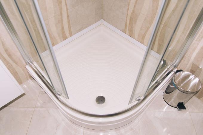 Looking down into a white quadrant shower tray with curved glass sliding doors and beige tiled walls.