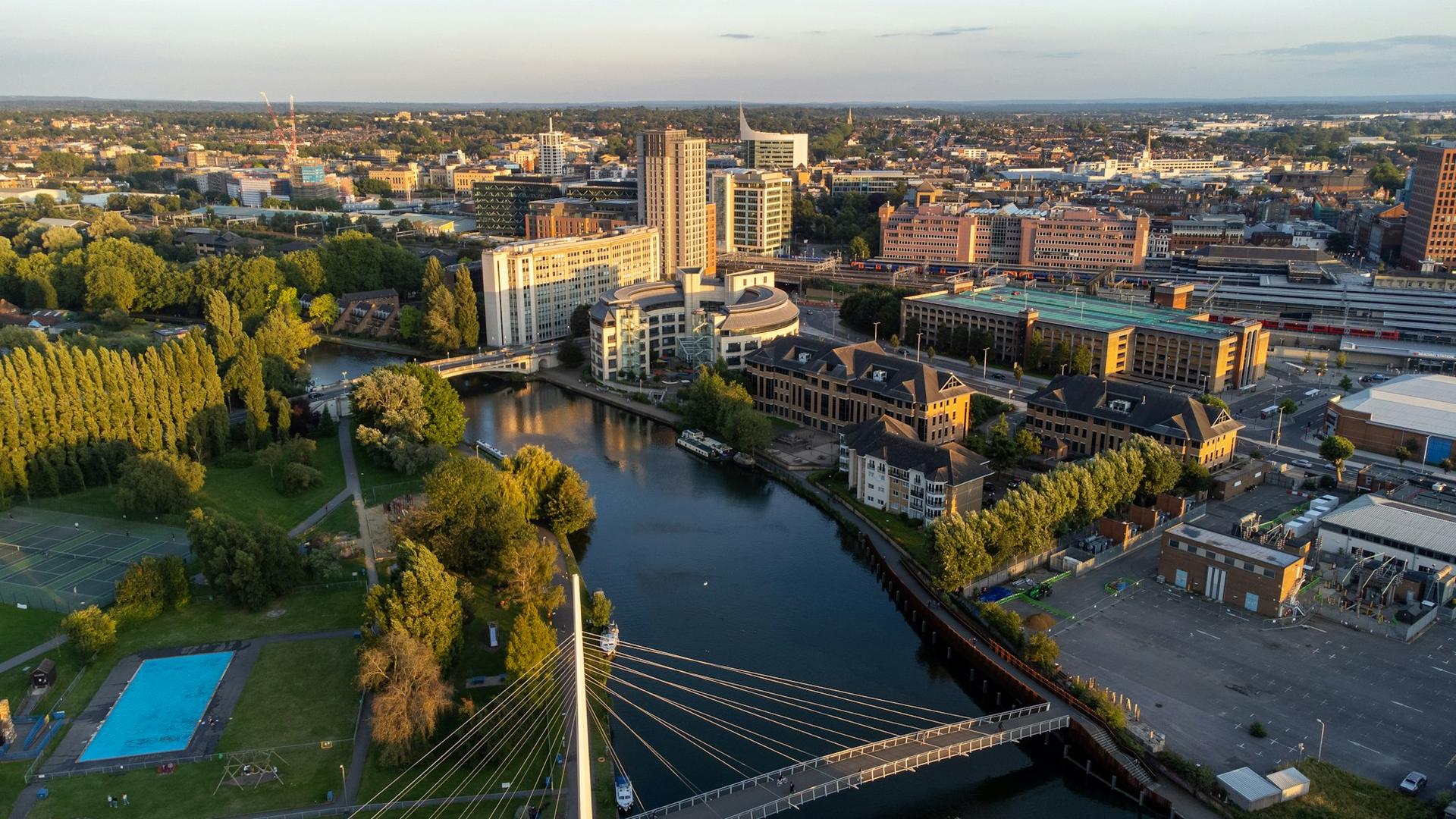 Aerial view of Reading at golden hour, with the Christchurch cable-stayed footbridge over the River Thames, riverside offices and the town centre beyond.