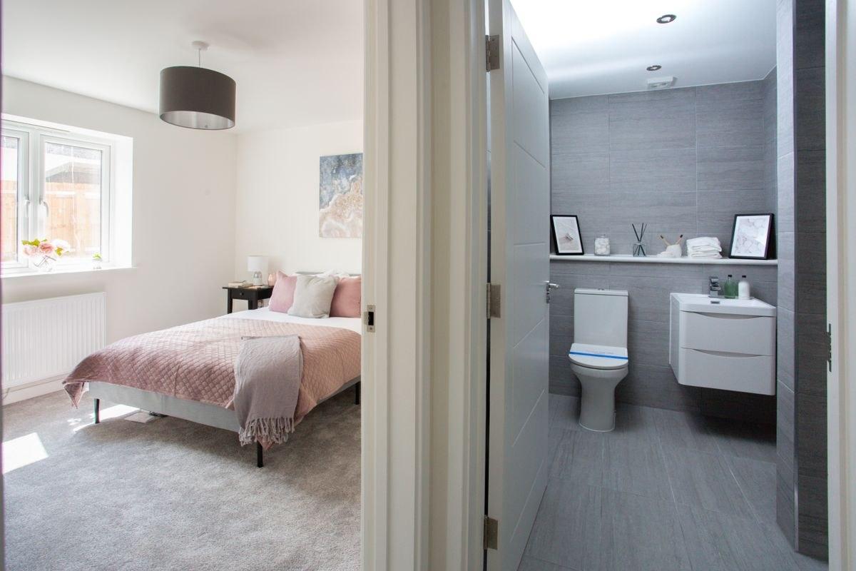 A white door frame and architrave between a bedroom and an en-suite, with the en-suite door open onto a toilet and a wall-hung basin.