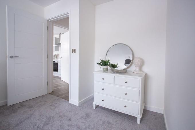 A carpeted bedroom with a white internal door and an open doorway showing its frame and architrave, beside a white chest of drawers and a round mirror.