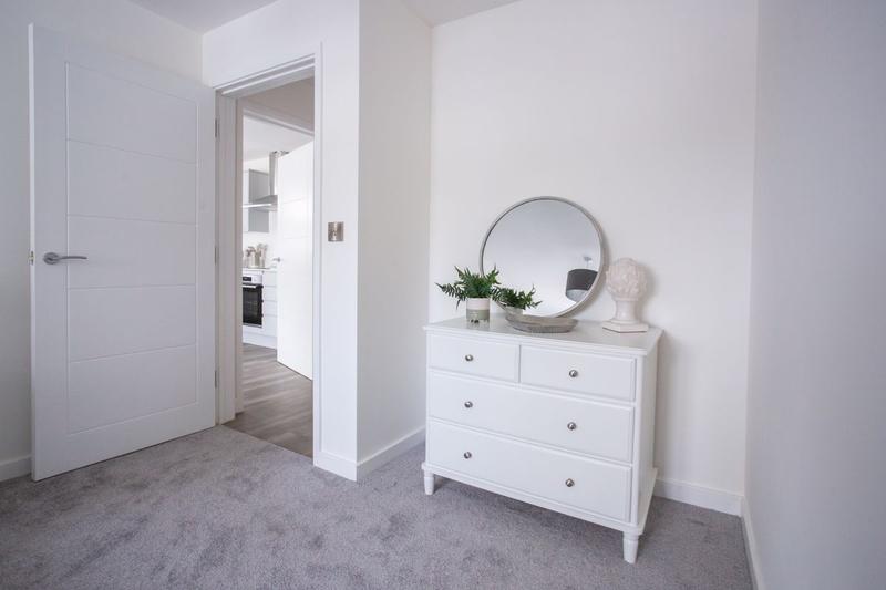 A carpeted bedroom with a white internal door and an open doorway showing its frame and architrave, beside a white chest of drawers and a round mirror.