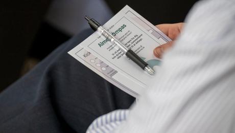 Papirer og kuglepen i hånden på siddende deltager til kickoff