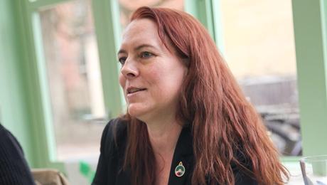 Kvinder sidder og lytter ved grønt bord med noter, glas og kopper